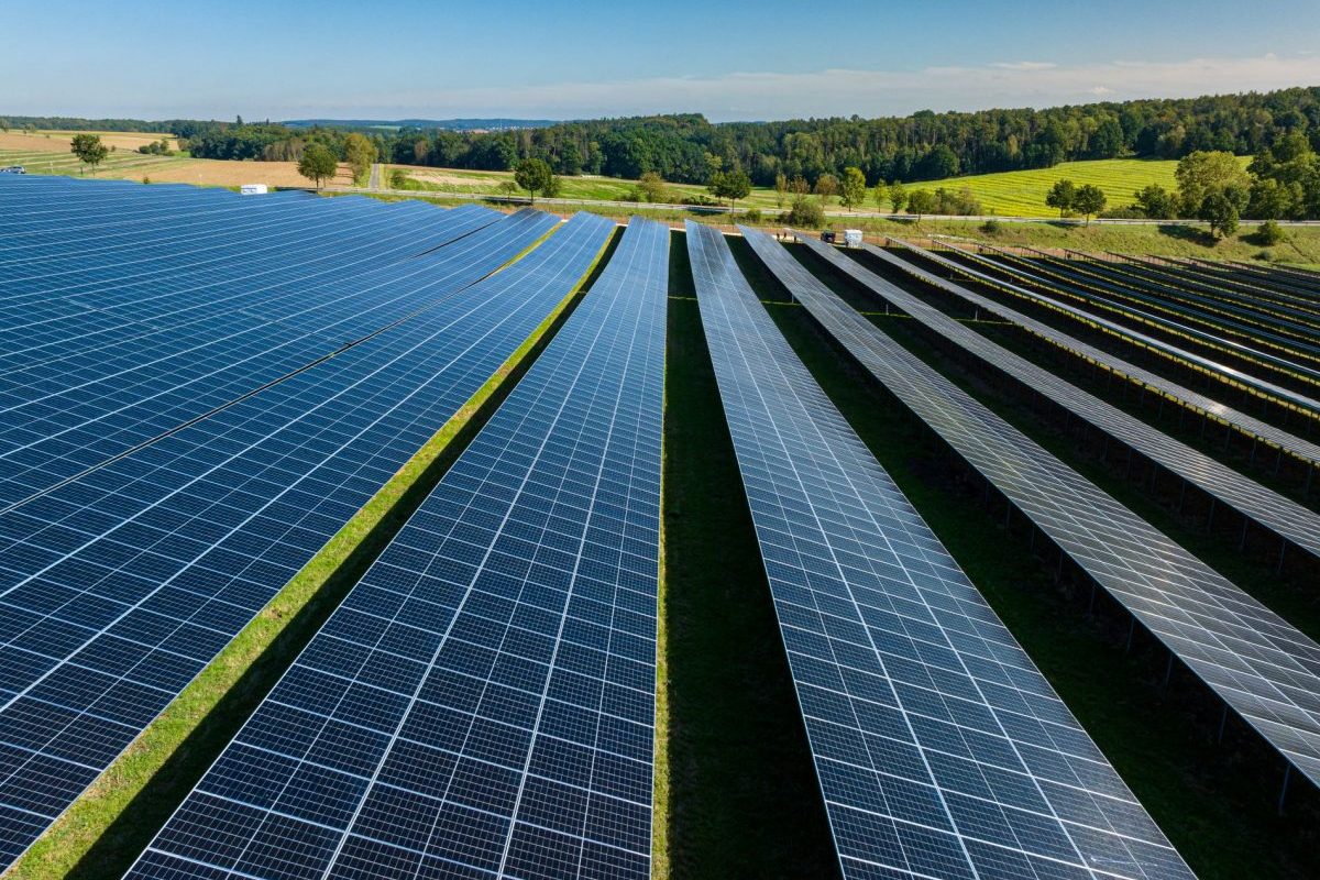 Aerial view of a ground-mounted PV system with module rows in a rural setting for reliable yield forecasts