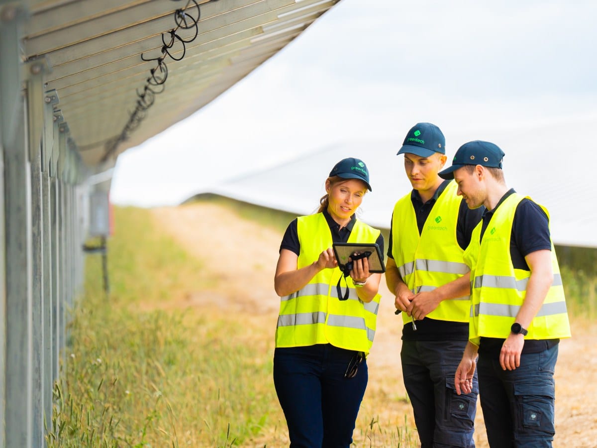 Ein greentech-Team führt eine technische Prüfung an einer Photovoltaik-Anlage durch und wertet dabei Daten auf einem Tablet aus.