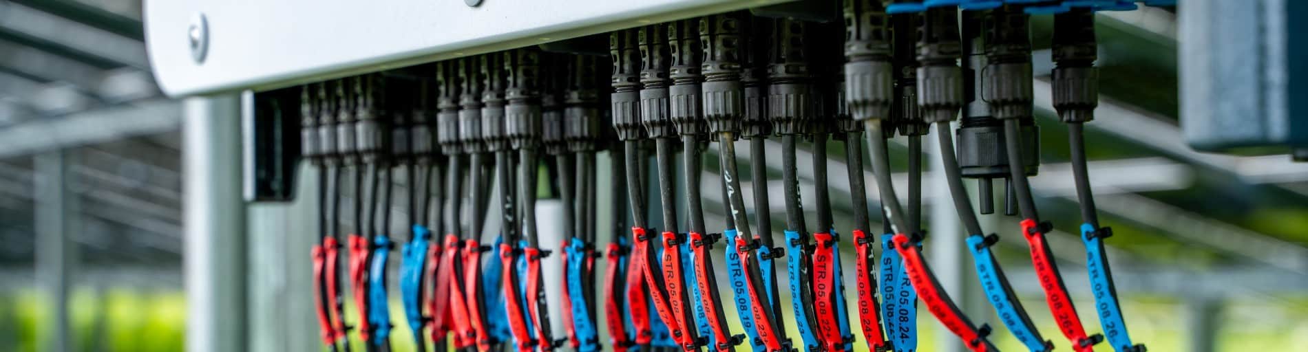 Nahaufnahme der DC-Stringverkabelung an einem Wechselrichter, die im Rahmen der technischen Prüfung einer PV- oder BESS-Anlage kontrolliert wird.