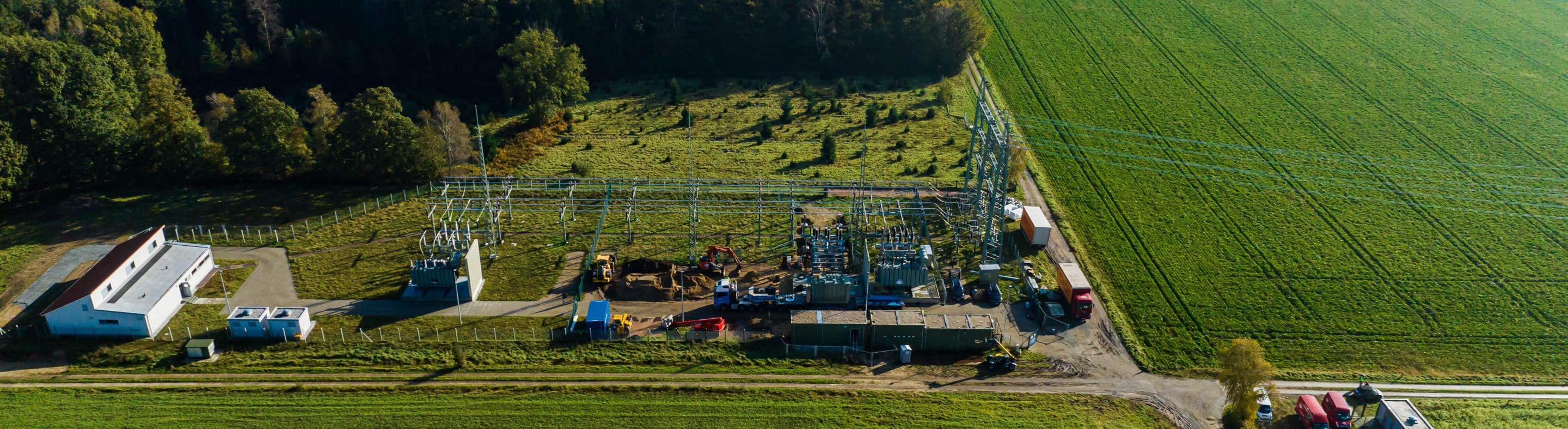 Luftaufnahme eines Umspannwerks in der Bauphase mit Transformatoren, Schaltanlagen und Baufahrzeugen auf grüner Fläche